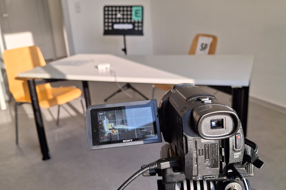 IKM erfolgreich durchgeführt Szene aus dem IKM-Testraum. Zusehen ist im Vordergrund eine Kamera, die eine Tisch mit zwei Stühlen aufnimmt, wo später die Teilnehmenden mit den Schauspielpatienten sprechen.